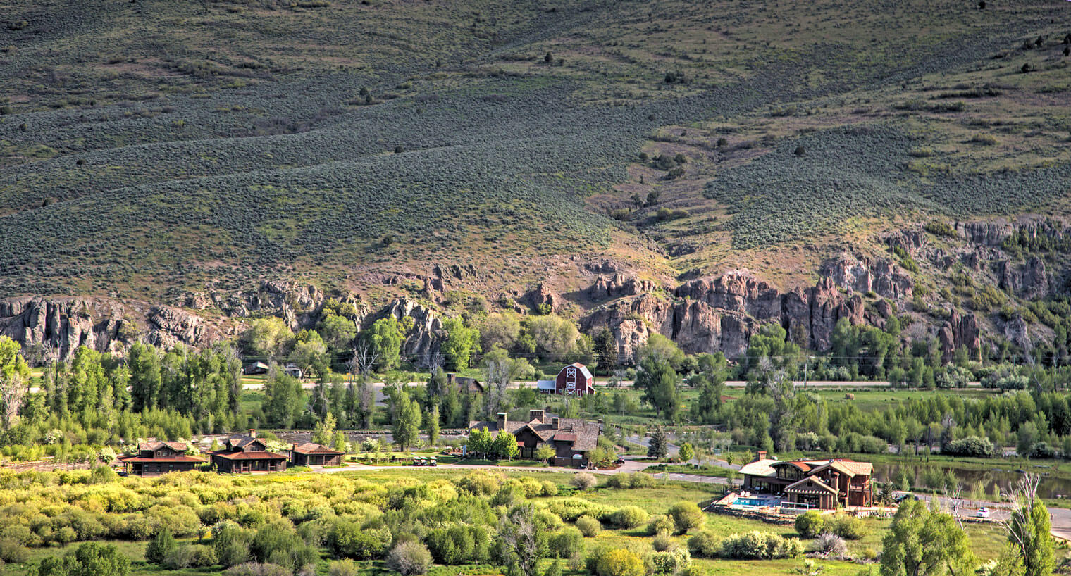 drone view of a lush mountain valley with a few houses and pond