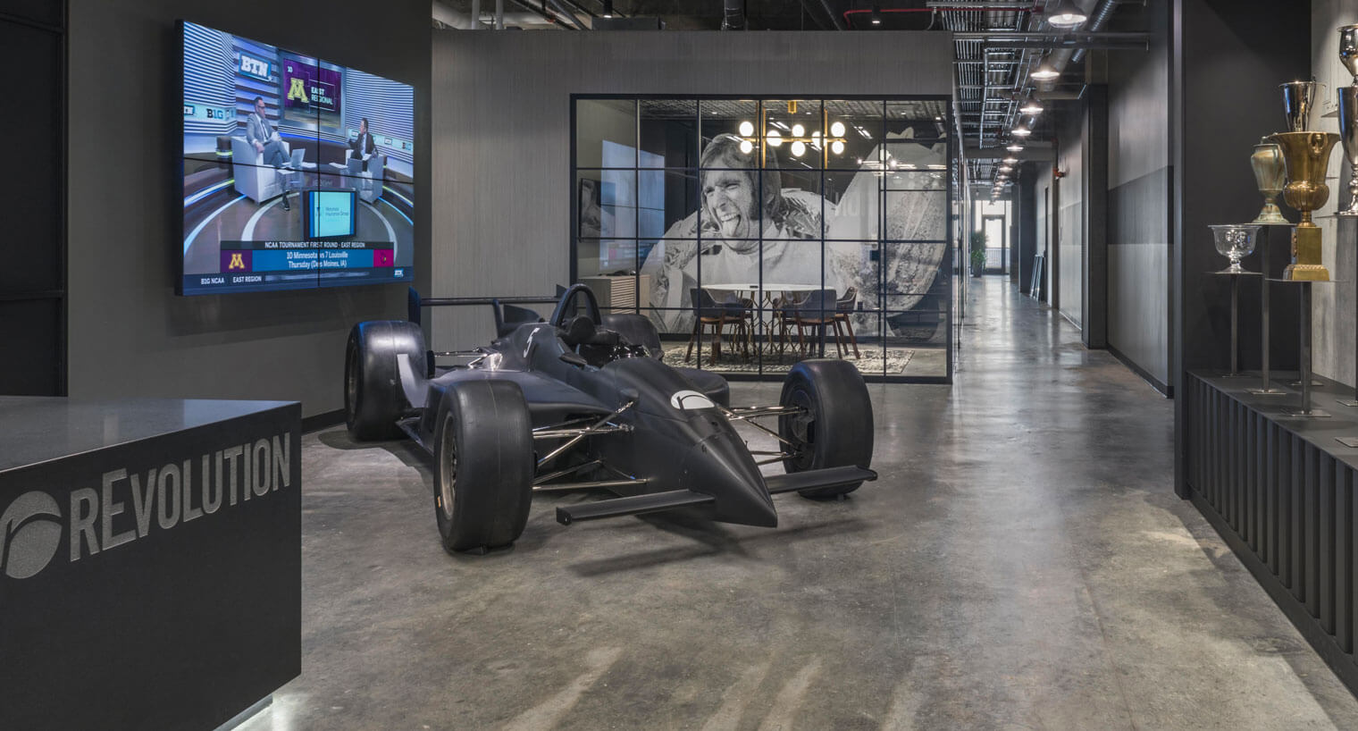 A racecar on display in industrial style lobby space with large TV screen