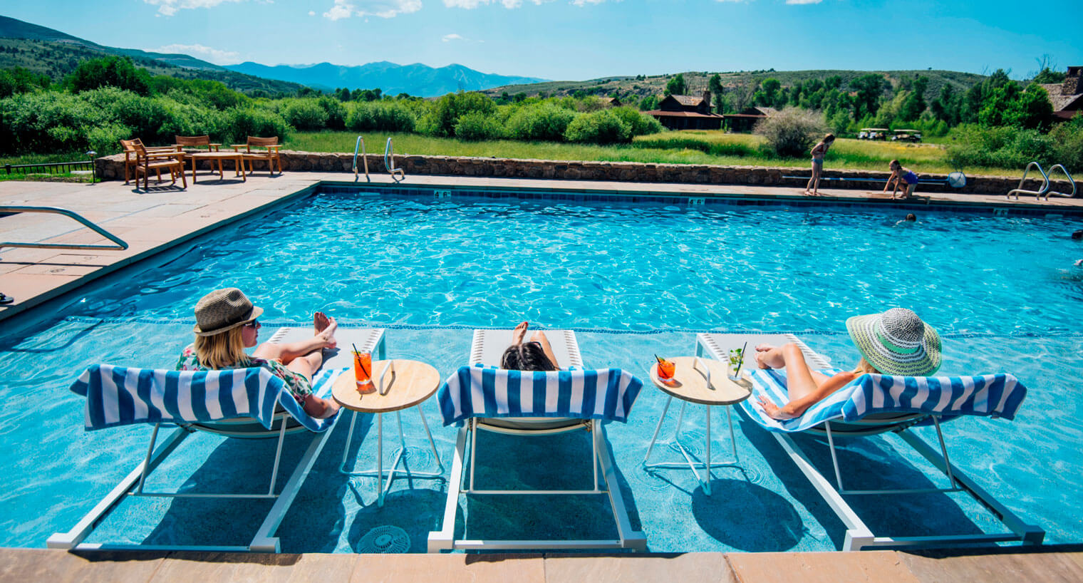 three women sitting in lounge chairs sipping cocktails by a pool