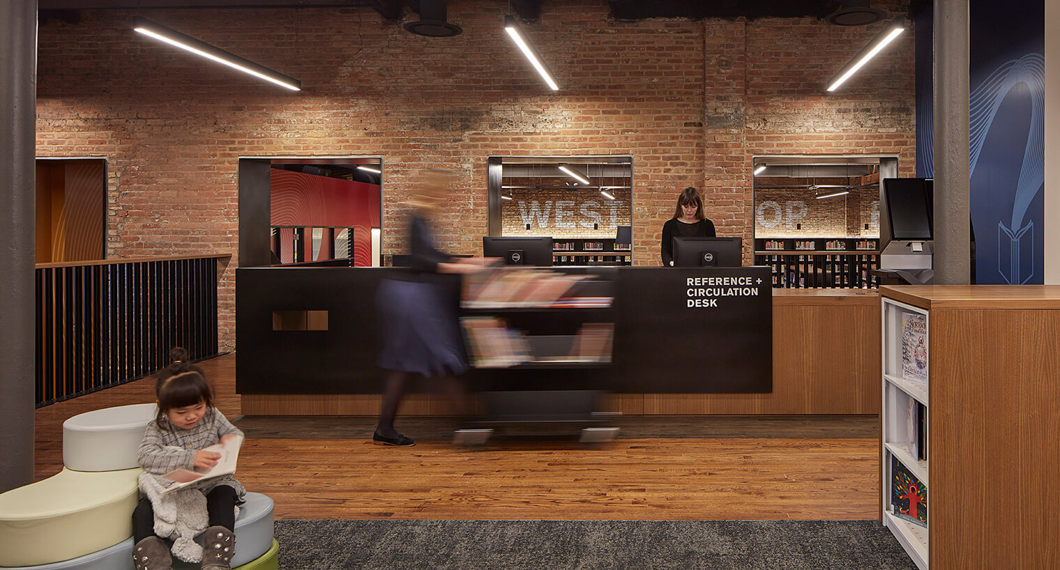 a kid reading infront of a reference and circulation desk